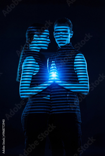 Young man and woman in darkness illuminated by blue horizontal neon light stripes. They hold hands, creating a bright glowing spark in the center.