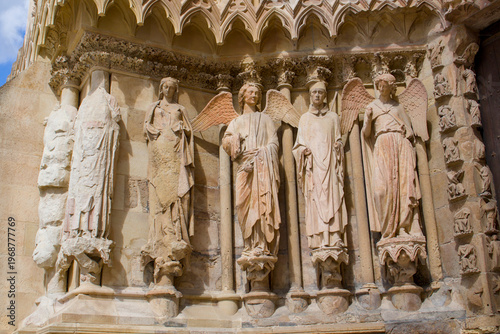 Stone saints and angels stand in quiet symmetry on the ornate facade of Reims Cathedral in France. Weathered sculptures reveal Gothic artistry through delicate carvings and serene expressions.