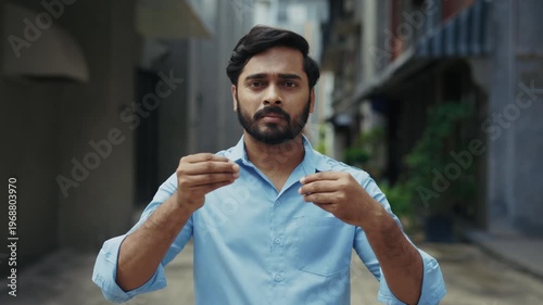 Portrait of bearded Indian man gesturing the phrase Say no to plastic in sign language in old city. Cheerful South Asian businessman communicating by gestures on street of town. Ecology concept.