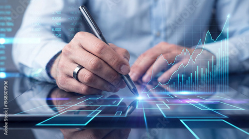 Close-up of male hands using a stylus on a digital tablet with glowing blue holographic financial graphs and data charts. Modern business technology.