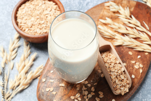 Oat milk in glass and flakes on grey textured table, closeup