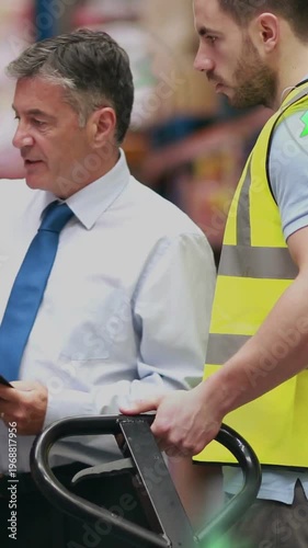 Vertical video: Manager pointing clipboard while worker gripping jack in warehouse, preparing stock