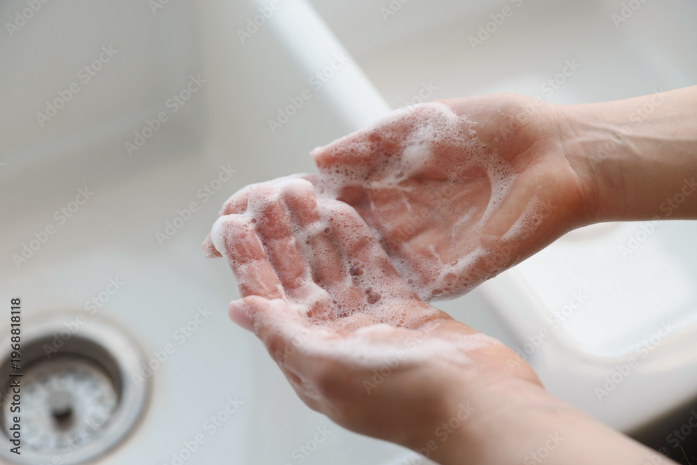 Fototapeta premium Woman washing hands with soap above white sink, closeup. Space for text