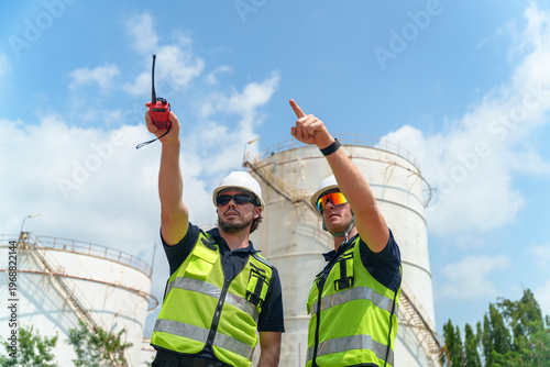 Tableau sur toile Two engineers in safety vests and hard hats discuss operations near industrial s