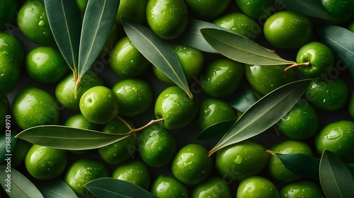 Fresh green olives with leaves arranged closely together on a dark surface, showcasing their natural sheen and vibrant color
