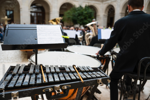 Photos Rear view of a percussionist in an orchestra, standing with mallets at a xylophone and timpani in an arched courtyard