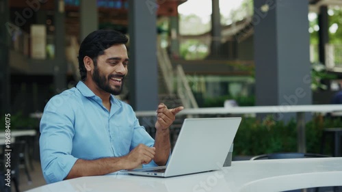 Portrait of happy Indian man using sign language on city street. Joyful bearded man smiling and saying Hi how are you I'm fine thanks. Communication and inclusion concept.