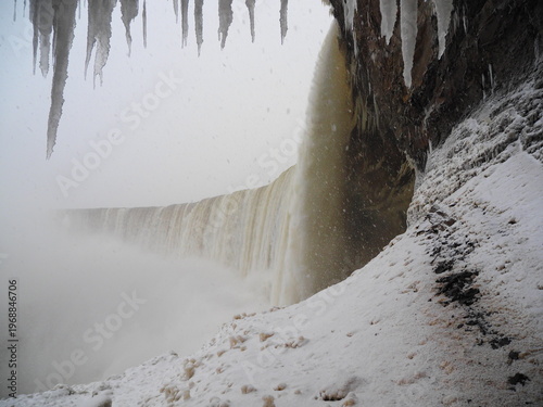 Winter waterfall beside snowy cliff and dark rock wall
