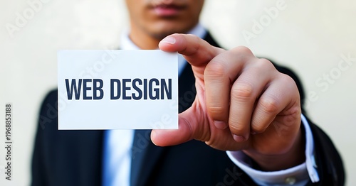 A close-up of a businessman's hand holding a card with the text 'WEB DESIGN' written on it, blurred suit and tie in the background.