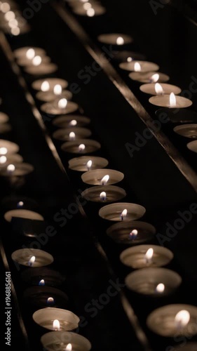 Close-up of rows of small candles burning in dark interior creating warm glowing lines of light. Camera remains static capturing soft flickering flames and calm atmospheric scene.