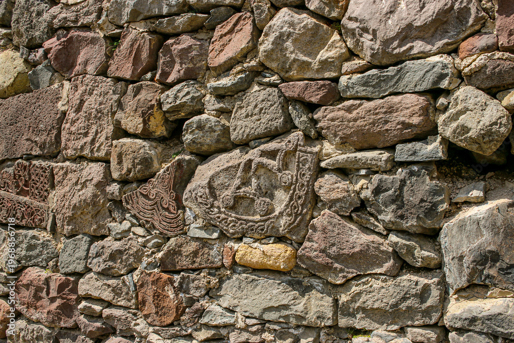 Fototapeta premium Ancient stone wall with carved ornaments and decorative elements, historic masonry texture and cultural heritage detail