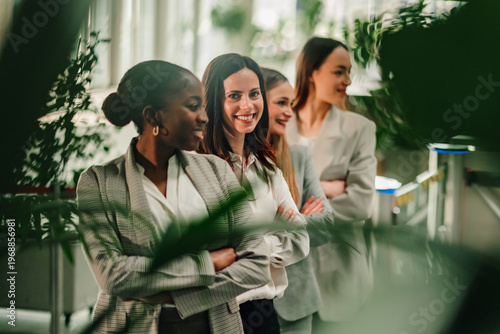 Diverse businesswomen team standing in line, smiling and showing confidence in a modern green office environment