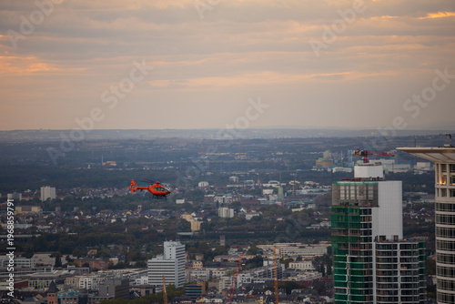 Orange rescue helicopter flying over Frankfurt am Main Innenstadt cityscape at sunset, Hessen, Germany
