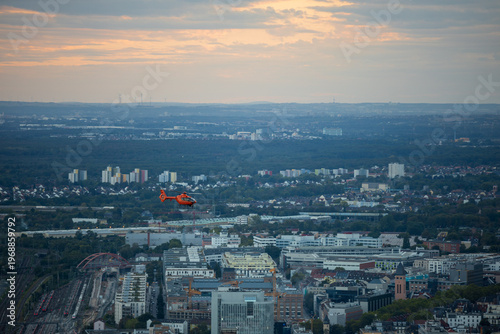 Orange rescue helicopter flying over Frankfurt am Main Innenstadt cityscape at sunset, Hessen, Germany, urban aerial view