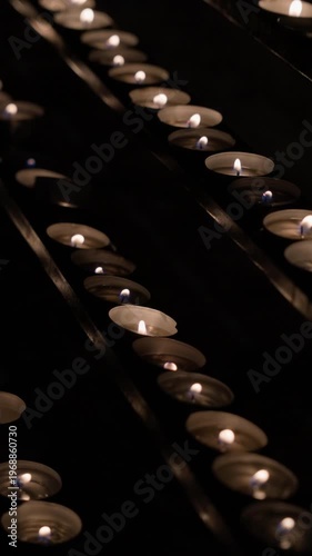 Close-up of multiple candle flames arranged in rows creating warm glowing light in dark interior. Camera remains static capturing soft flickering fire and calm atmospheric scene.