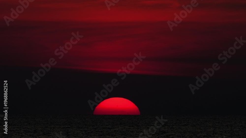 Golden sunset over the sea, captured from a scenic viewpoint. The sun slowly dips below the horizon, casting warm orange and yellow tones. Peaceful and serene atmosphere