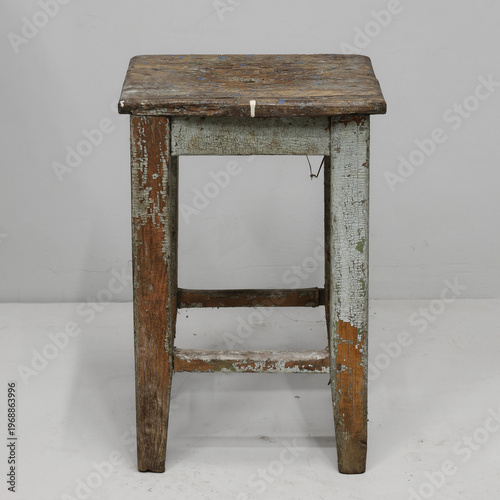 Old wooden stool with a rustic charm and faded colors stands alone against a neutral background, showcasing its vintage appeal