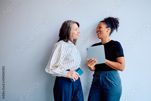 Fotografia Two diverse business women laughing, communicating, and interacting while using