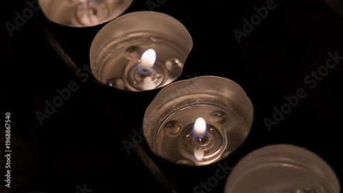 Close-up of several candles burning in a row with soft warm light and shallow depth of field. Static camera captures gentle flickering flames and calm atmospheric interior scene.