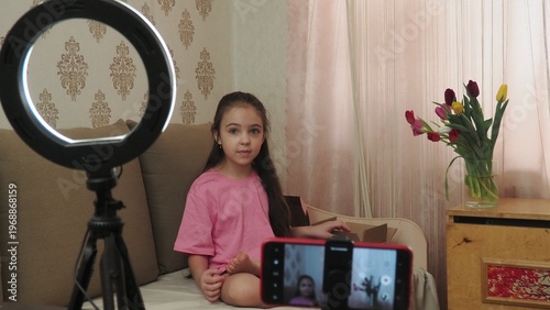 A beauty blogger, a girl dressed in a pink T-shirt, applies eye patches, films videos about her daily skincare routine, and reviews cosmetic products on social media. She films the videos on her phone