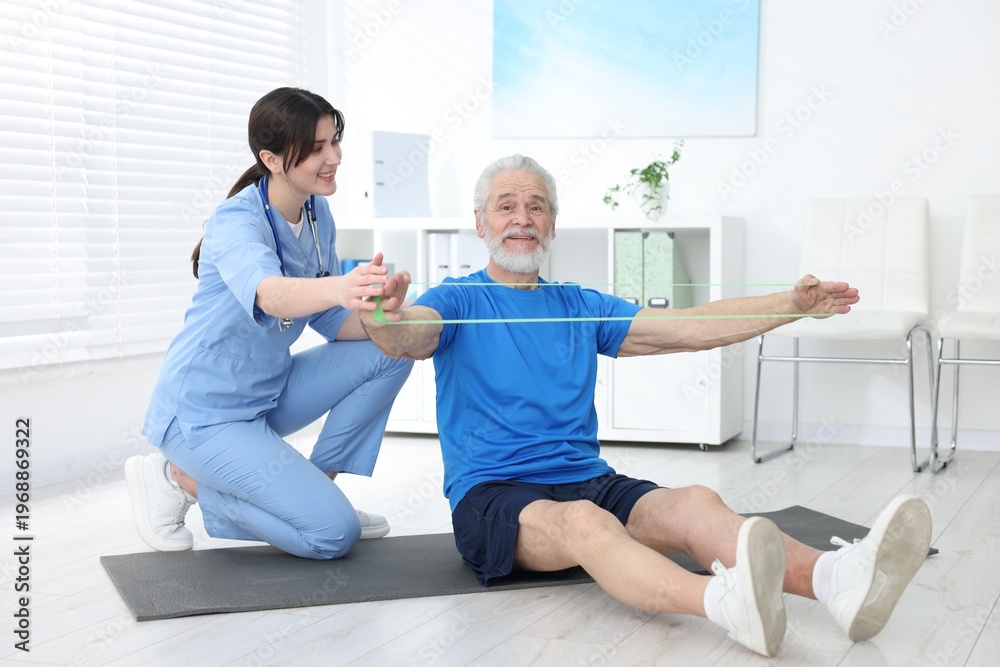 Fototapeta premium Senior man training with resistance band under physiotherapist supervision indoors
