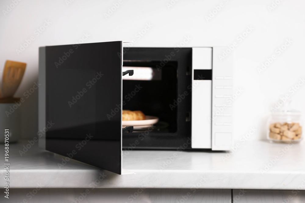 Fototapeta premium Modern microwave with cooked crepes on countertop in kitchen, closeup