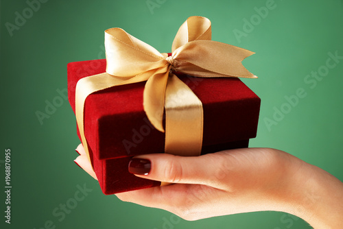 Woman holding elegant gift box with golden bow against green background, closeup