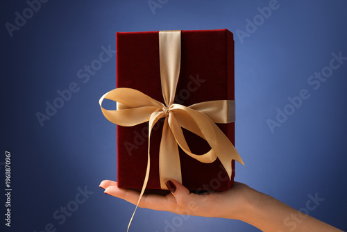 Woman holding beautiful gift box against blue background, closeup