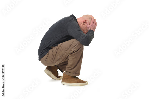 side view of a stressed man squatting looking down hands on face