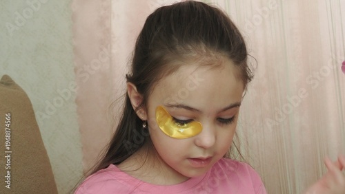 A beauty blogger, a girl dressed in a pink T-shirt, applies eye patches, films videos about her daily skincare routine, and reviews cosmetic products on social media. She films the videos on her phone