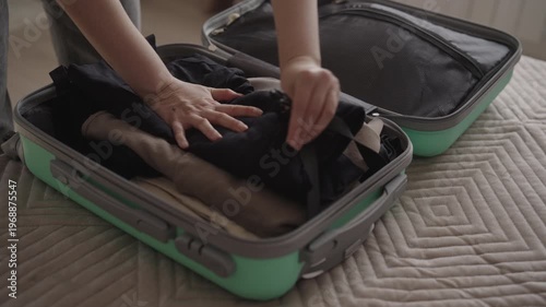 Closeup of young woman packing clothes into suitcase, folding items, struggling to close full luggage by sitting on it before trip at home or hotel., slow motion Concept of travel organization.