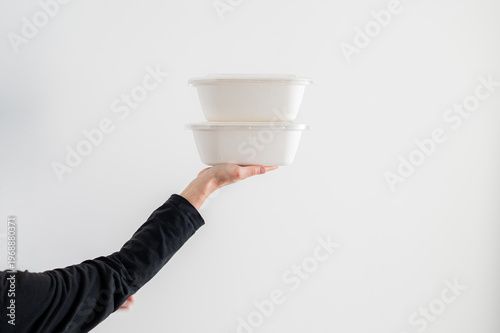 Una mujer sostiene dos envases de comida para llevar de cartón reciclado, aislados sobre fondo blanco. Concepto de packaging alimentario, delivery y consumo responsable.