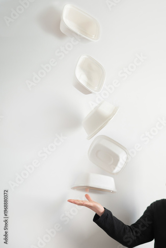 Varios envases de comida para llevar de cartón, flotando en el aire. Una mujer lanza envases de delivery. Concepto de packaging alimentario y consumo responsable. Fotomontaje.