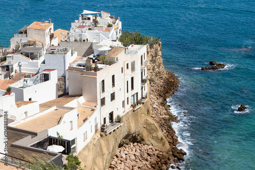 Whitewashed residential buildings on a rocky cliff overlooking the sea on the Spanish island of Ibiza.