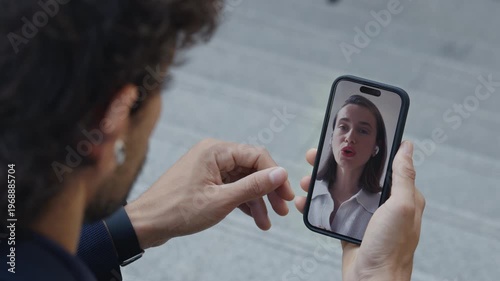 Man hand holds mobile phone at video call with female colleague on city street closeup. Woman manager explains project details to partner during online meeting via smartphone