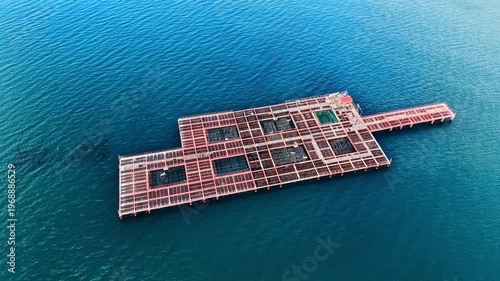 Aerial view of a red industrial mussel farm structure on calm blue water. Large metal floating platform for aquaculture in the sea.