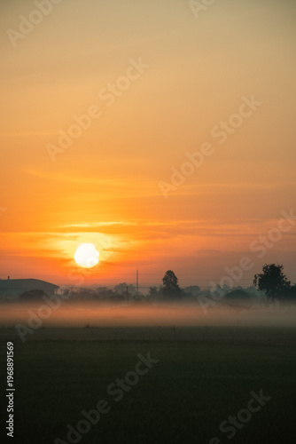Sunrise over misty countryside with industrial silhouettes — a serene blend of nature and structure