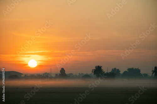 Sunrise over misty countryside with industrial silhouettes — a serene blend of nature and structure