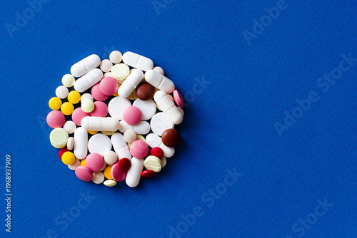 A circle of pills on the left side of the photo. Capsules and pills of different sizes and colors on a blue background. Photo with space for text