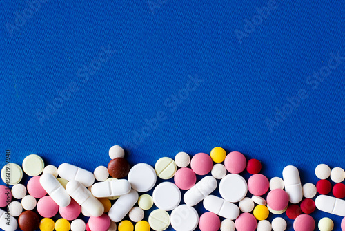 Heap of colorful tablets, capsules and pills at the bottom of the background. Line of tablets on a blue background. Place for text. Pharmacology and medicine