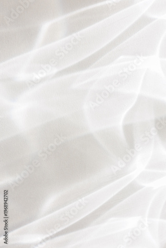 Ethereal white light caustics and shimmering water reflections create a clean, minimalist abstract pattern on a bright textured wall surface. Stock photo