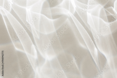Ethereal white light caustics and shimmering water reflections create a clean, minimalist abstract pattern on a bright textured wall surface. Stock photo