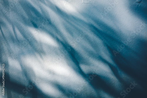 Dramatic sunlight creates natural leaf shadows on a textured blue wall, perfect for organic background or overlays designs and moody aesthetic concepts. Stock photo