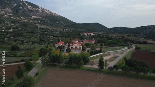 Monastery nestled in a valley with olive groves and a church.