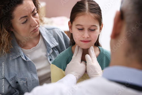 Photos Endocrinologist in medical gloves examining girl's thyroid gland while her smili