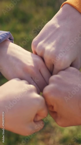 Four fists are coming together in a playful gesture on a grassy field. The fists display camaraderie and connection among the individuals participating in this gesture.