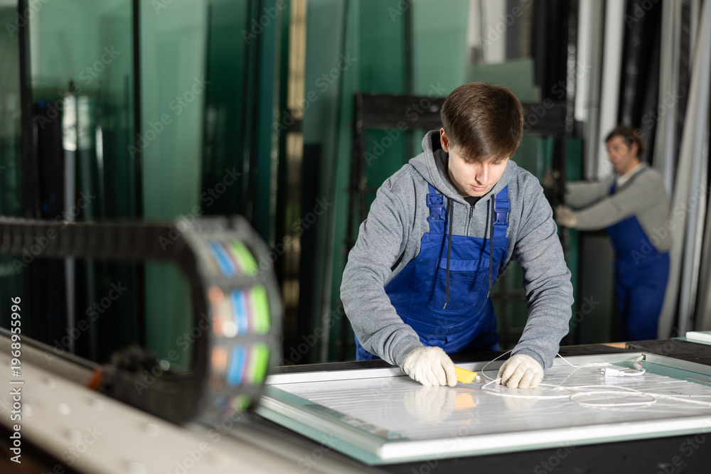 Fototapeta premium In workshop for production of glass products, guy co-worker cuts off excess from workpiece and finishes creating plastic panel. .