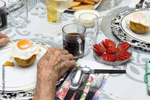 Close-up of senior man’s hand preparing to eat Ecuadorian bolón mixto with fried egg, traditional food