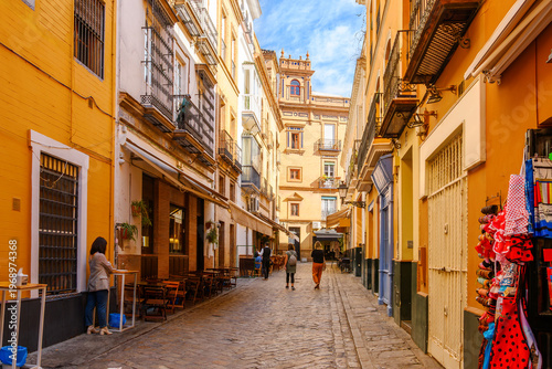 Εκτύπωση καμβά A colorful cobblestone side street in the historic Barrio Santa Cruz district, with sidewalk cafes and souvenir shops in the Andalusian city of Seville, Spain