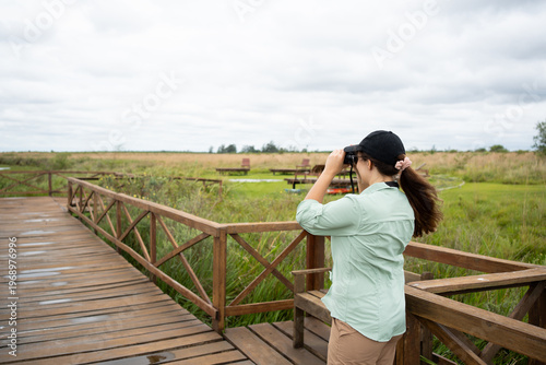Woman birdwatching with binoculars on a wooden boardwalk